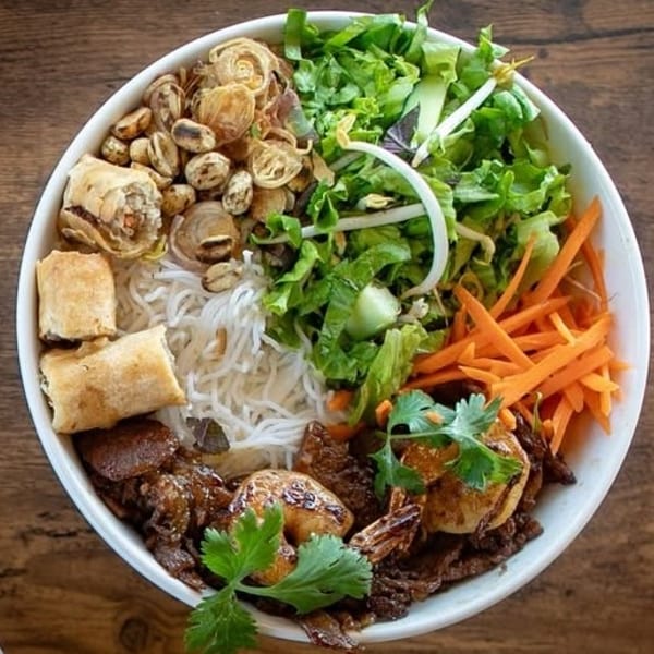 A colorful Vietnamese vermicelli bowl with spring rolls, shrimp, beef, vegetables, and noodles.