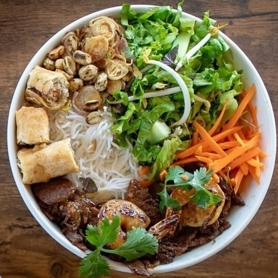 A colorful Vietnamese vermicelli bowl with spring rolls, shrimp, beef, vegetables, and noodles.