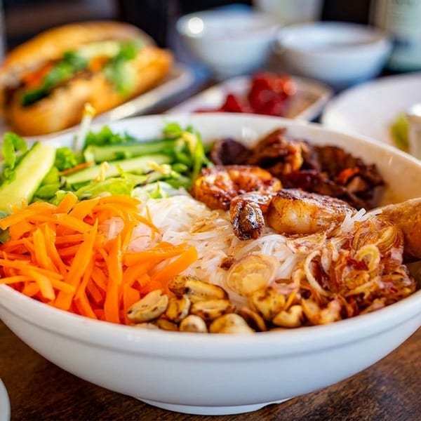 A Vietnamese vermicelli bowl with grilled shrimp, egg roll, vegetables, and peanuts.