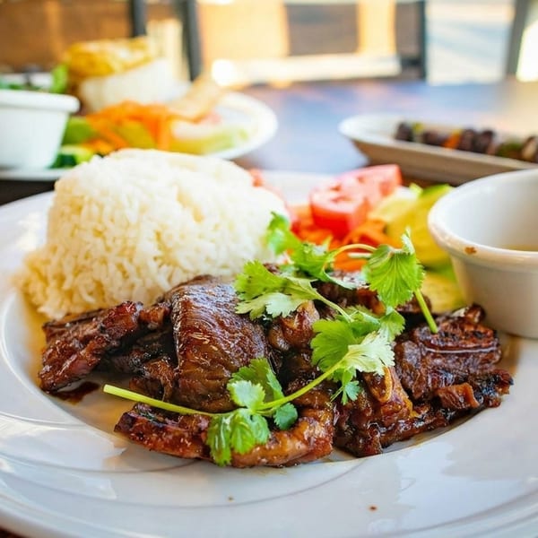 Grilled meat with rice, fresh cilantro, and vegetables on a white plate, with other dishes blurred in the background.