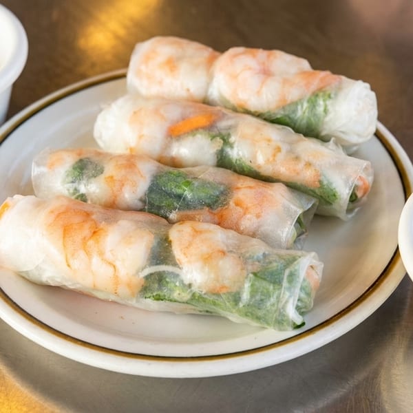 Four fresh shrimp spring rolls with vegetables on a plate, served with two bowls of peanut sauce.
