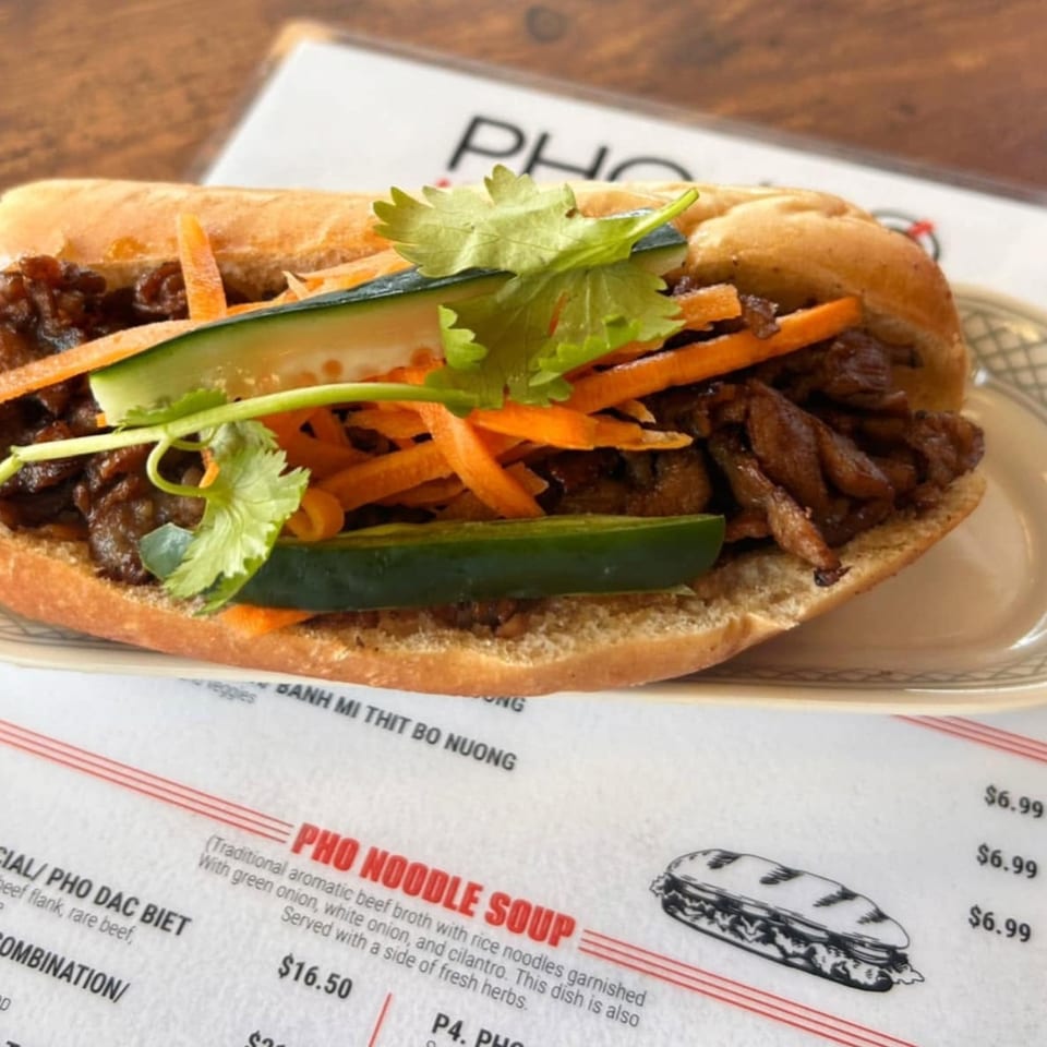 A delicious banh mi sandwich with grilled beef, pickled carrots, cucumbers, and cilantro on a plate.